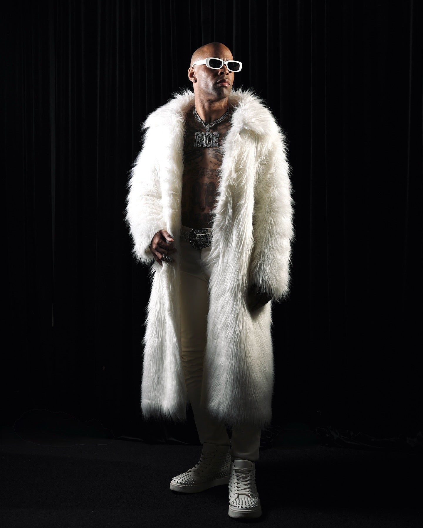 Person wearing a white fur coat and sunglasses on a black background